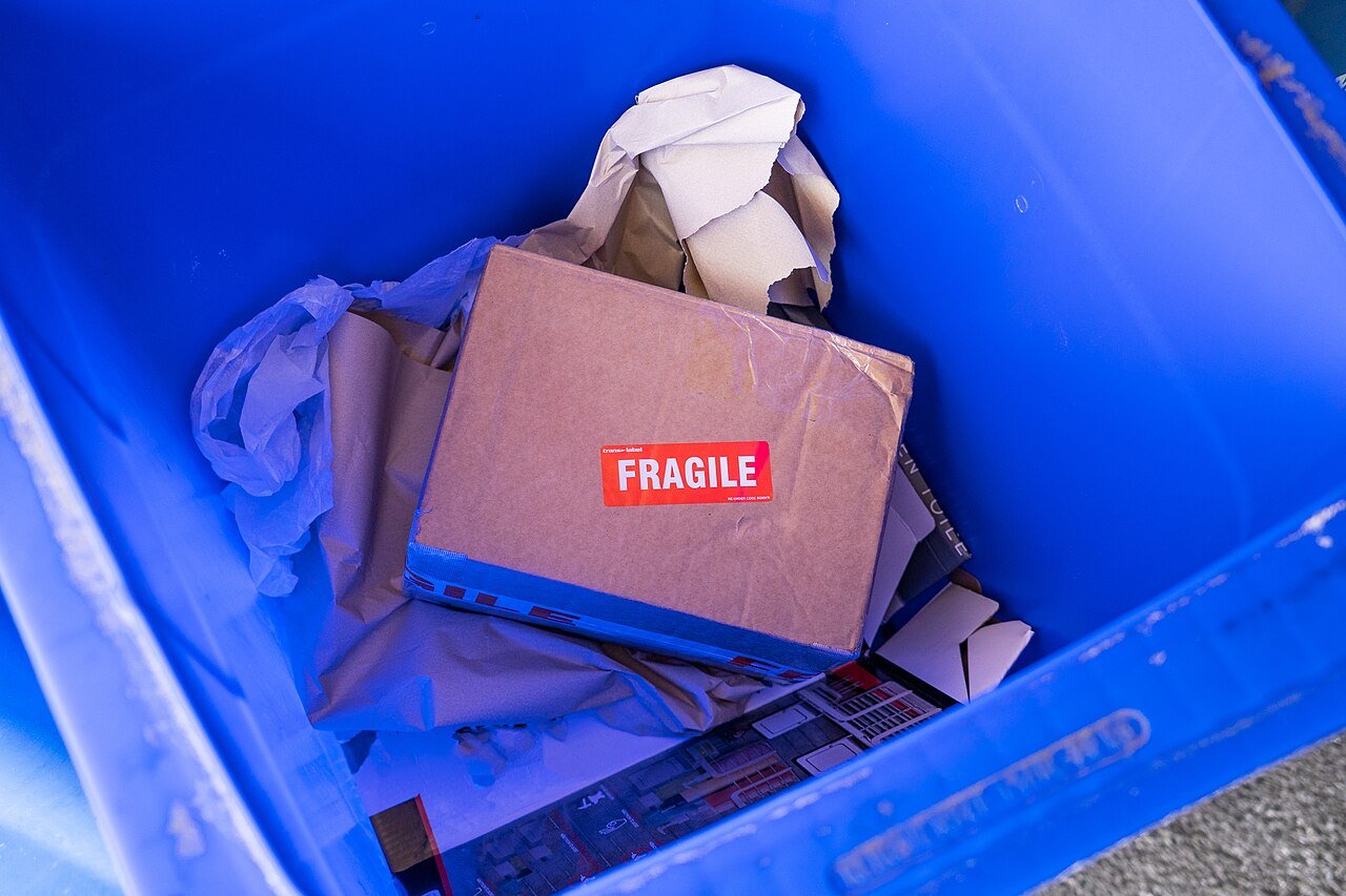 Cardboard packaging containing unsuitable material inside a blue recycling bin